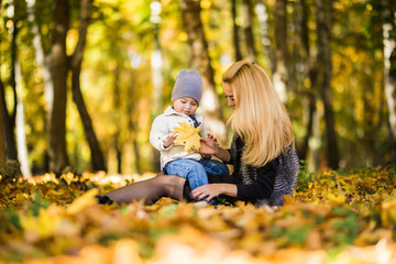 Happy family mother playing with child in autumn park near tree lying on yellow leaves. Autumn concept.