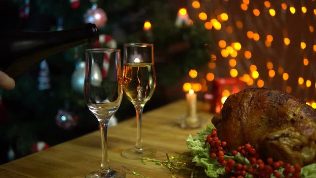 A roasted bird on a platter with a salad next to a glass of champagne stands on a table amidst yellow electric lights with a festive Christmas dinner in the evenings.