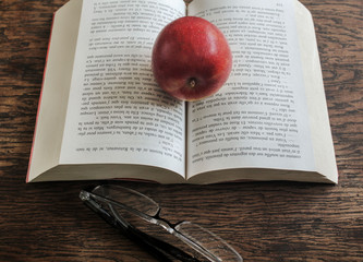 red apple resting on the book with glasses on the table
