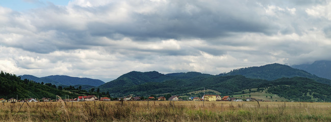 A typical natural landscape of Romania: fields, a small lake and a village of houses with red roofs, mountains on the horizon. Panoramic view.