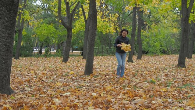 A woman collects yellow leaves in an autumn park.