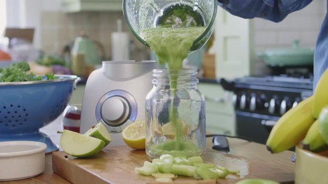 Woman Pouring Green Smoothie In Jar From Blender At Kitchen
