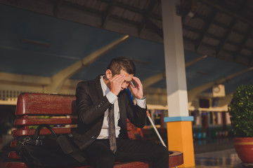 Young asian businessman feel stressed/worry/headache/disappoint during working 
while sit at train station, vintage photo and film style.