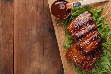 Closeup of pork ribs grilled with BBQ sauce and caramelized in honey on a bed of arugula. Tasty snack to beer on a wooden Board for submission on the old wooden background. Top view with copy space