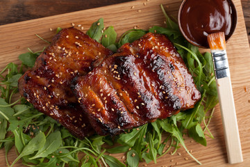 Closeup of pork ribs grilled with BBQ sauce and caramelized in honey on a bed of arugula. Tasty snack to beer on a wooden Board for submission on the old wooden background. Top view
