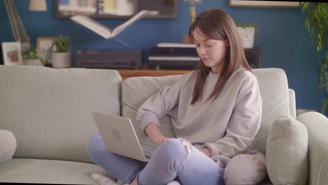 Female Blogger Using Laptop While Sitting On Sofa At Home
