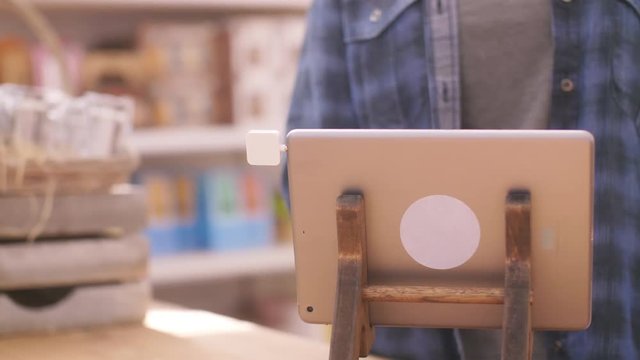 Deli Owner Using Square Chip Reader Connected To Digital Tablet