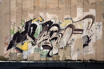 A fragment of detailed graffiti of a drawing made with aerosol paints on a wall of concrete tiles. Background image of street art in brown and cream tones