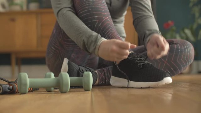 Low Section Of Fit Woman Tying Shoe Lace By Dumbbells