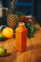 Plastic bottle with orange carrot juice and fruits on the wooden table. Close up
