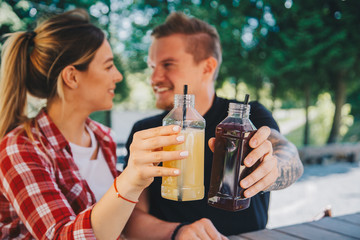 Young couple drinking healthy detox juice from plastic bootles outdoors in cafe. Close up. Fruit and vegetables pressed juice
