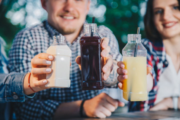 Close up fresh detox fruit and vegetable juice concept. Friends holding plastic bottles with pressed juice. Garden, outdoor