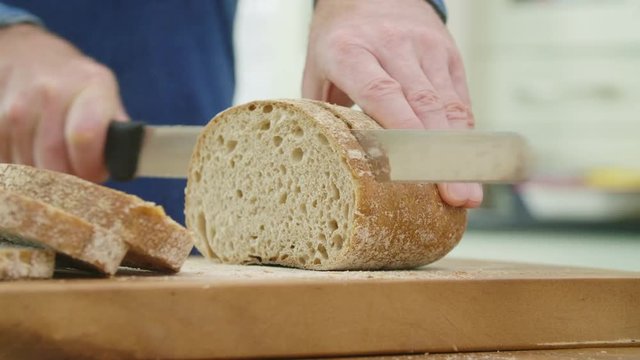 Man Slicing Loaf Of Bread With Knife On Cutting Board
