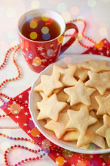 Plate with cookies shaped like star, cup of tea, christmas decorations