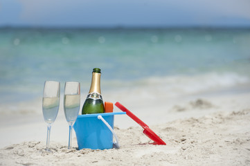 champagne and glasses in sand bucket on tropical beach