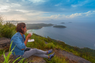 Fototapeta premium a lady drinking coffee on the highest viewpoint name Pha Hin Dum. on Pha Hin Dum viewpoint can see around Phuket island. Niharn beach wind turbine Phomphep cape Rawai beach are in front of Pha Hin Dum