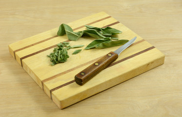 Fresh sage leaves and chopped sage on wooden cutting board with kitchen knife