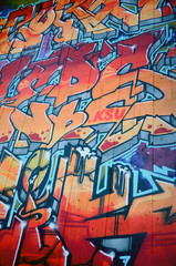 A fragment of detailed graffiti of a drawing made with aerosol paints on a wall of concrete tiles. Background image of street art in warm red color tones