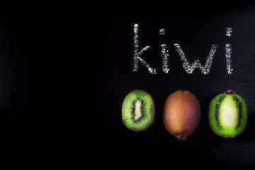 Kiwi on a black background. Cut and whole fruit of kiwi lying on a black wooden table. White word written with chalk on a blackboard. Flat lay. Food concept. A place for your inscription.