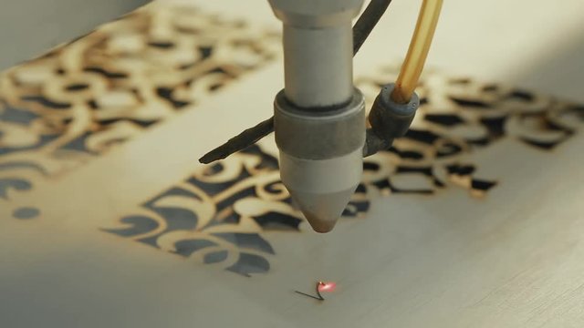 Machine for laser cutting wood close up cuts chipboard and the smoke appears. The red beam.