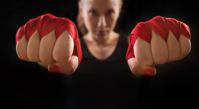 Female boxer is showing hands with red wraps, macro shot, black background. Women self defense. - Powered by Adobe