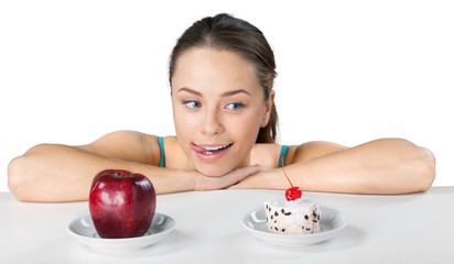 Attractive young woman makes her choice between apple and cake