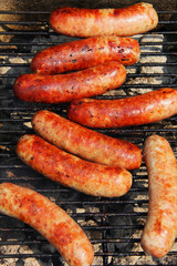Fototapeta premium Bratwursts on a grill. Close up composition of grilled outdoor brat sausages during good weather 4th of July picnic. Lifestyle background, unhealthy eating concept.. Vertical composition.