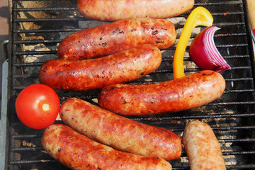 Bratwursts on a grill. Close up composition of grilled outdoor brat sausages during good weather 4th of July picnic. Lifestyle background, unhealthy eating concept.