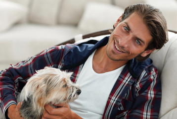 handsome guy stroking his dog while sitting in a large armchair.