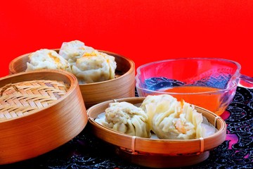 Steamed dumplings served in bamboo containers with chili sauce in red background