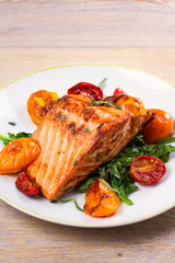 Salmon fillet with spinach and tomatoes on white plate on rustic wooden background