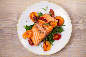 Salmon fillet with spinach and tomatoes on white plate on rustic wooden background. Overhead, top view