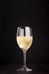 Wine glass with white wine on elegant dark black wooden background, copy space, vertical. Template for portfolio, advertising, design, branding identity, cover magazine, bar and restaurant menu.