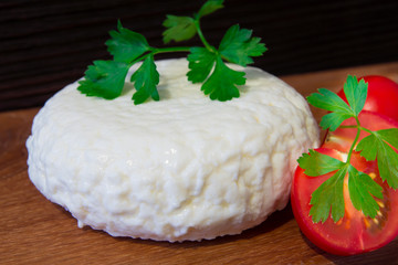 Fresh cheese with excellent taste and aroma. Cheese on wooden cutting Board with tomatoes and fresh herbs.