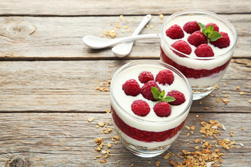 Dessert with raspberries and granola in glasses on grey wooden table