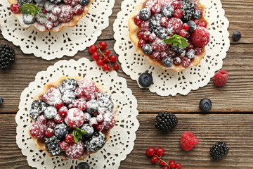 Tasty tartlet with berries and powdered sugar on grey wooden table