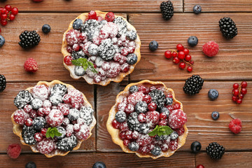 Tasty tartlet with berries and powdered sugar on brown wooden table