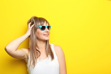 Portrait of young woman with sunglasses on yellow background