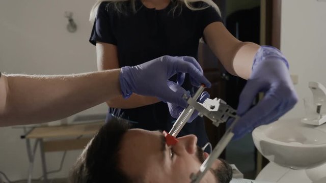 The orthodontist applies a face boy to his patient to achieve a more successful cosmetic effect during the treatment of teeth. Installation of the face-bow