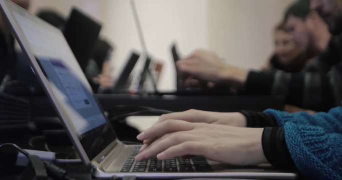 Female hands close-up of a typing on a laptop while on a background group of people with gadgets gathering at table