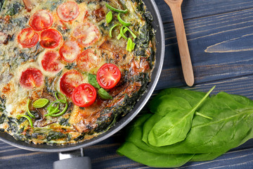 Frying pan with delicious spinach frittata on wooden background