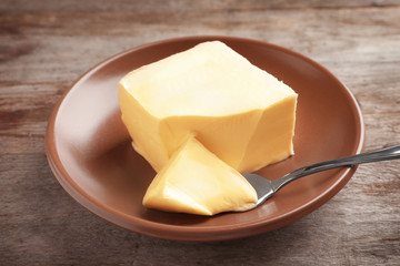 Plate with block of butter on wooden background