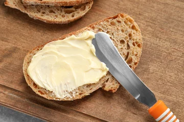 Gardinen Slice of bread with butter on wooden board © Africa Studio