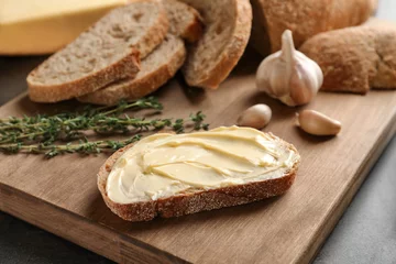 Rolgordijnen Slice of bread with butter on wooden board © Africa Studio