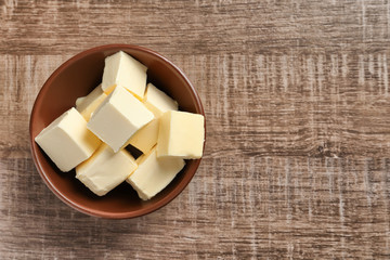 Bowl with cubes of butter on wooden background