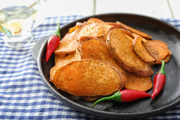 Frying pan with yummy sweet potato chips on table