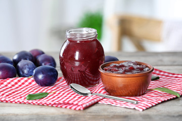 Bowl and jar of delicious plum jam on table