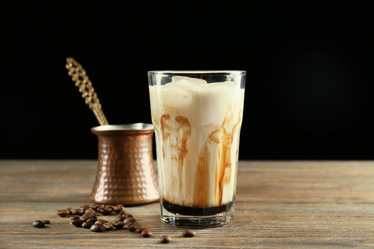 Glass with iced latte macchiato on wooden table against black background