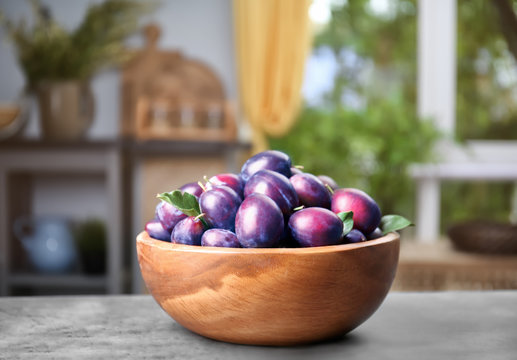 Fresh plums in wooden bowl on table