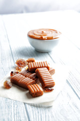 Sweet caramel candies and bowl with sauce on wooden table